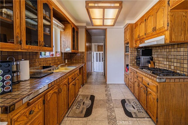 kitchen featuring tile counters, under cabinet range hood, light tile patterned floors, stainless steel appliances, and a sink