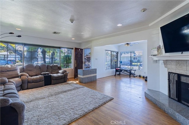 living room featuring a ceiling fan, wood finished floors, visible vents, a tile fireplace, and a textured ceiling