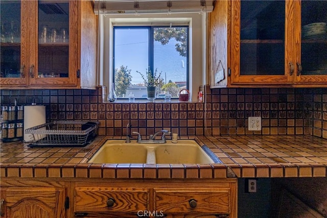 kitchen featuring tile counters, brown cabinetry, tasteful backsplash, and a sink