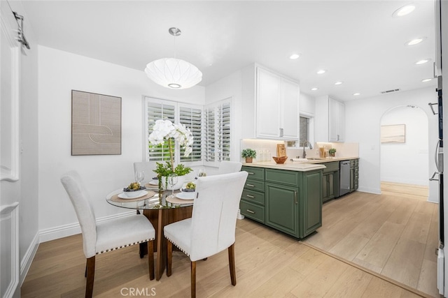 kitchen with a sink, white cabinets, light countertops, light wood-type flooring, and green cabinetry