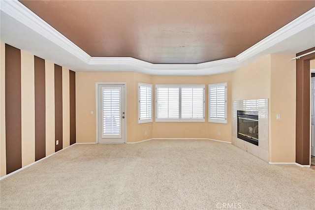 unfurnished living room with light carpet, baseboards, a tiled fireplace, a raised ceiling, and crown molding