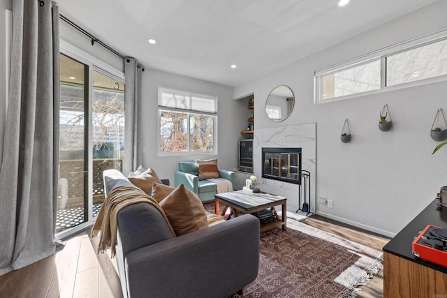 living area with recessed lighting, wood finished floors, a wealth of natural light, and a high end fireplace