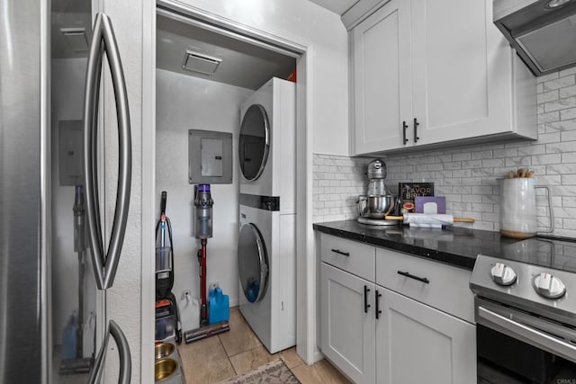 kitchen with appliances with stainless steel finishes, white cabinetry, stacked washing maching and dryer, and exhaust hood