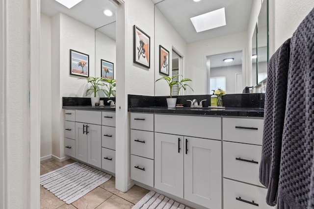 full bath with a sink, a skylight, and two vanities