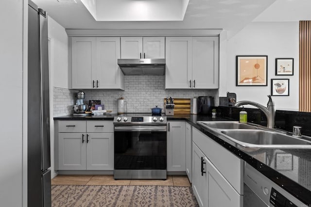 kitchen featuring decorative backsplash, stainless steel appliances, under cabinet range hood, a sink, and light tile patterned flooring