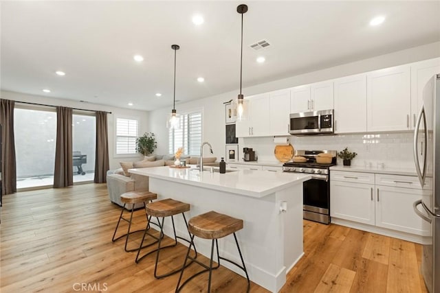 kitchen featuring appliances with stainless steel finishes, a kitchen island with sink, decorative light fixtures, and white cabinetry