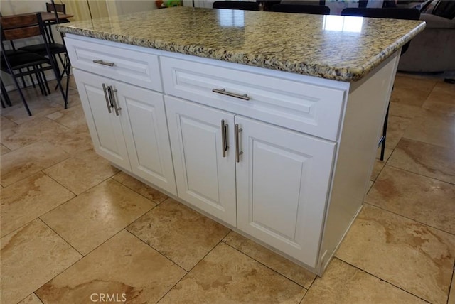 kitchen view of a center island, light stone counters, and white cabinetry