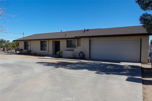 ranch-style house with a garage, concrete driveway, roof with shingles, and stucco siding