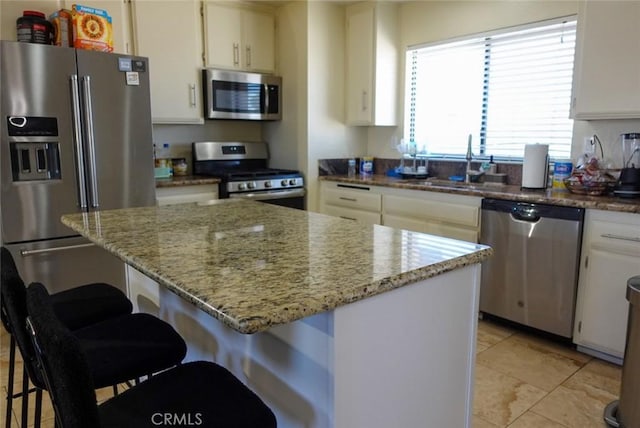 kitchen featuring stainless steel appliances, a sink, a kitchen bar, white cabinetry, and light stone countertops