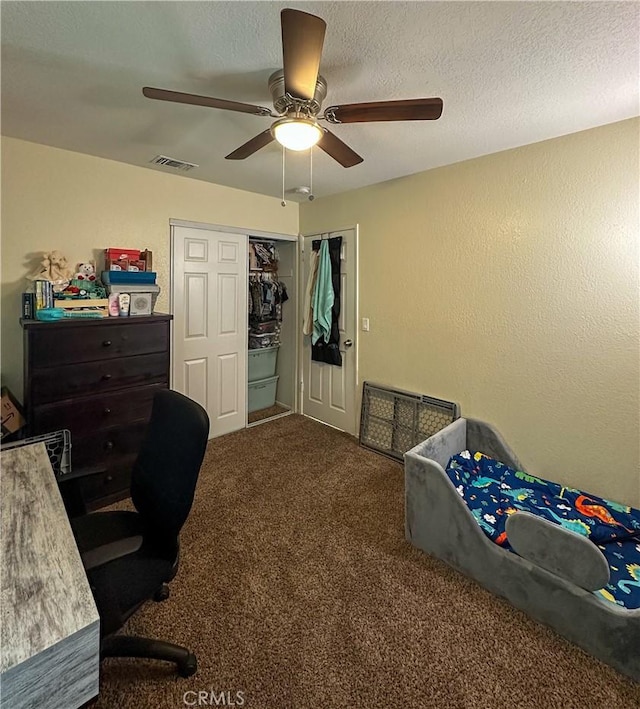 carpeted bedroom with ceiling fan, an office area, a closet, and a textured wall