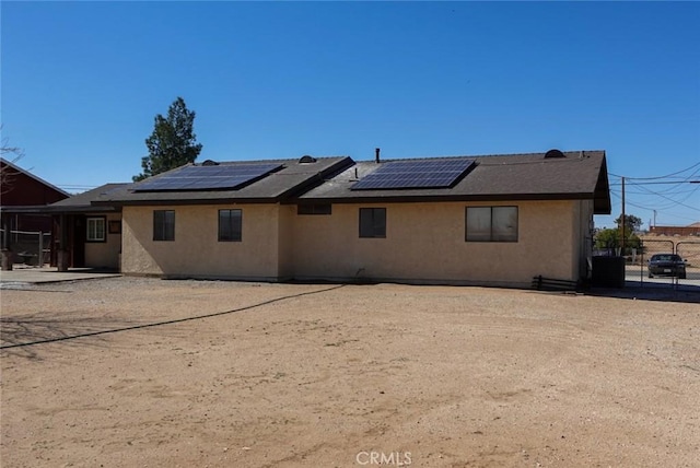 rear view of property with stucco siding, solar panels, and fence