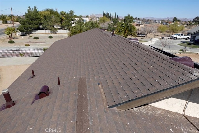 exterior view of a shingled roof, fence, and a mountain view