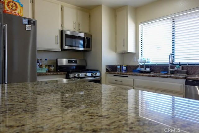 kitchen featuring appliances with stainless steel finishes, a sink, light stone counters, and white cabinets