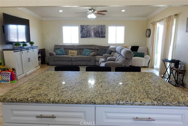 kitchen with ornamental molding, healthy amount of natural light, light stone countertops, and ceiling fan