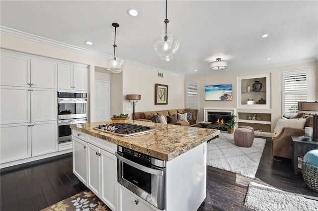 kitchen featuring white cabinets, open floor plan, hanging light fixtures, appliances with stainless steel finishes, and light stone countertops