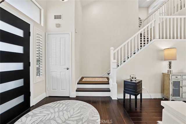 foyer featuring a towering ceiling, stairs, baseboards, and dark wood-style flooring