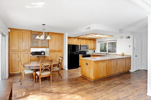 kitchen featuring visible vents, decorative light fixtures, a peninsula, light countertops, and black appliances