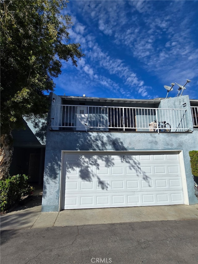 townhome / multi-family property with driveway, a balcony, an attached garage, and stucco siding