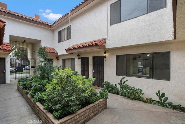 entrance to property with a tiled roof, stucco siding, a gate, and fence