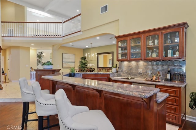 bar featuring light wood finished floors, tasteful backsplash, visible vents, decorative light fixtures, and wet bar