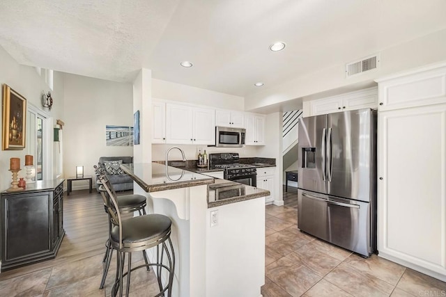 kitchen with a breakfast bar area, stainless steel appliances, visible vents, white cabinets, and a peninsula