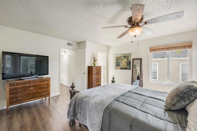 bedroom with a textured ceiling, dark wood-style flooring, visible vents, and a ceiling fan