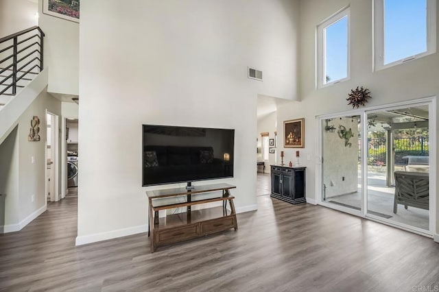 living area featuring wood finished floors, visible vents, baseboards, stairway, and washer / dryer