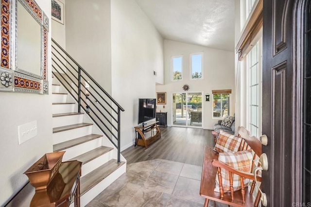 foyer entrance with stairs, high vaulted ceiling, wood finished floors, and baseboards