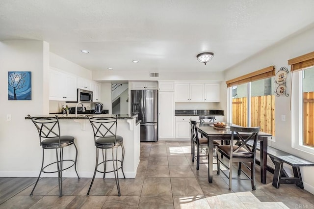 kitchen featuring stainless steel appliances, visible vents, white cabinets, dark stone counters, and a kitchen breakfast bar