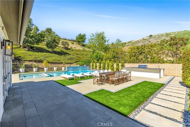 view of pool with an outdoor kitchen, a patio, a fenced backyard, outdoor dining area, and a pool with connected hot tub