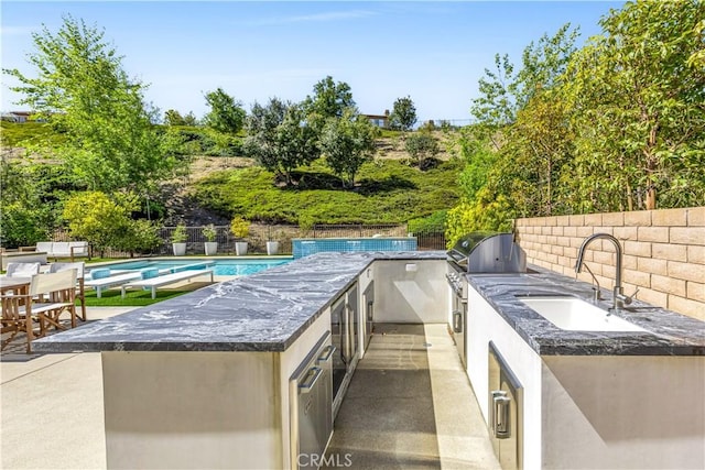 view of patio with an outdoor kitchen, a fenced in pool, a fenced backyard, grilling area, and a sink