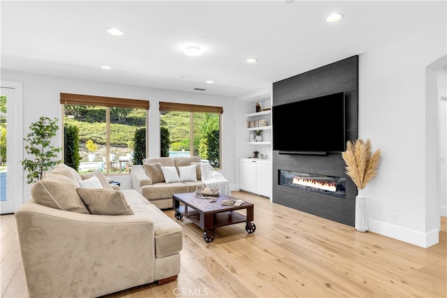 living room featuring built in shelves, a fireplace, recessed lighting, light wood-type flooring, and baseboards