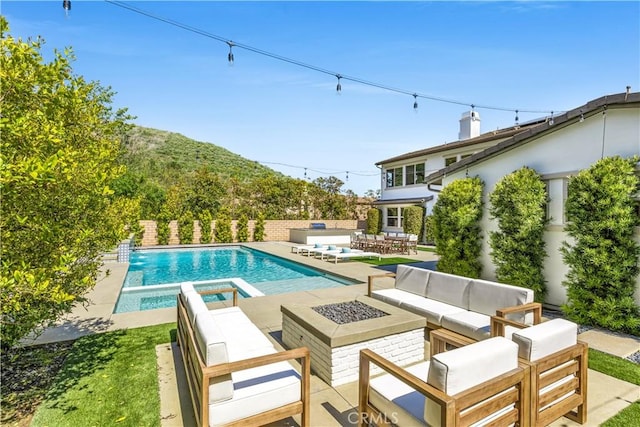 view of swimming pool featuring a pool with connected hot tub, a patio, and an outdoor living space with a fire pit