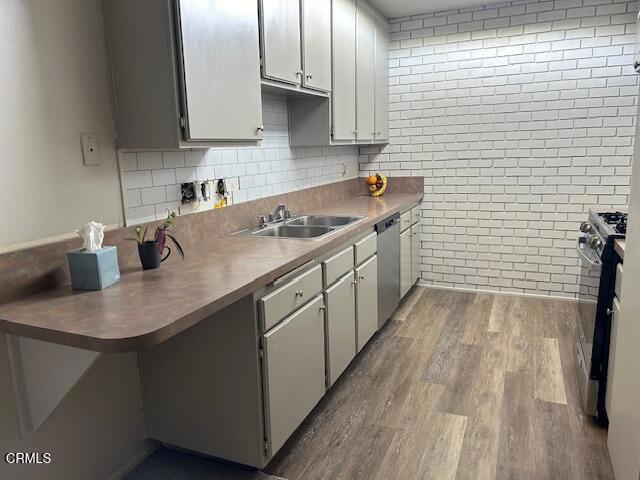 kitchen with white cabinets, brick wall, appliances with stainless steel finishes, wood finished floors, and a sink