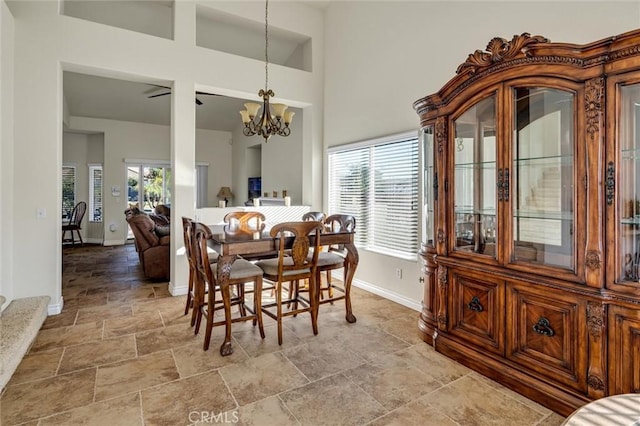 dining room featuring baseboards, stone finish floor, a towering ceiling, and an inviting chandelier