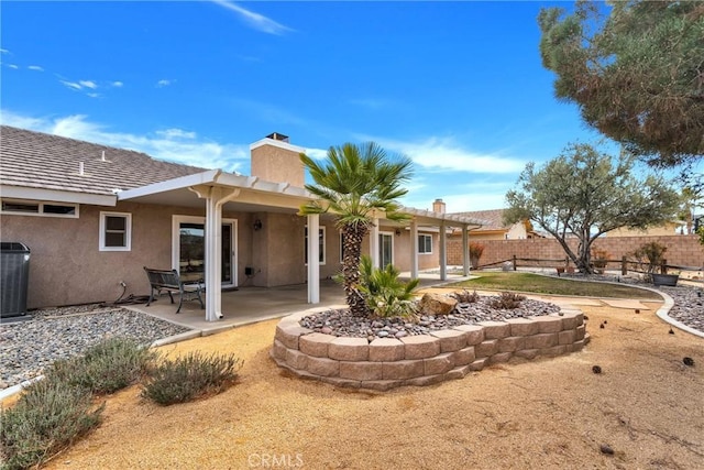 rear view of property with central AC unit, a chimney, fence, a patio area, and stucco siding