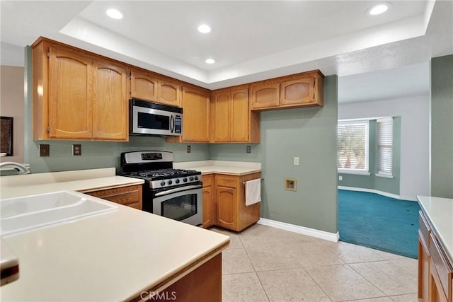 kitchen with light countertops, appliances with stainless steel finishes, brown cabinetry, and a sink