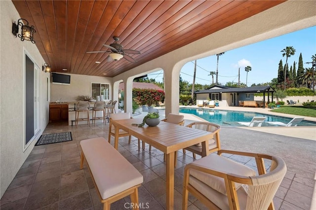 view of patio / terrace with outdoor dry bar, an outdoor pool, a ceiling fan, and an outdoor structure