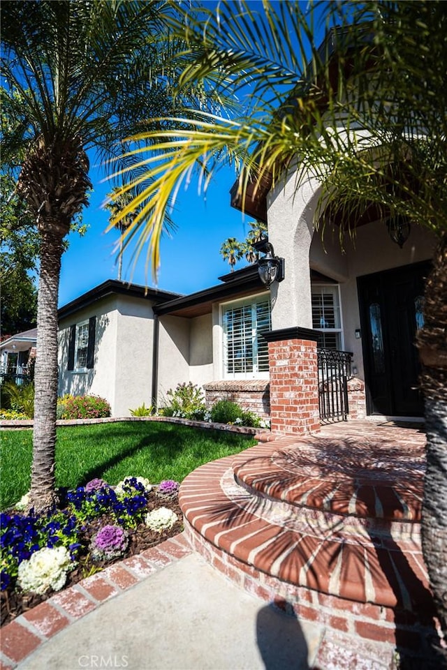 entrance to property featuring a lawn and stucco siding
