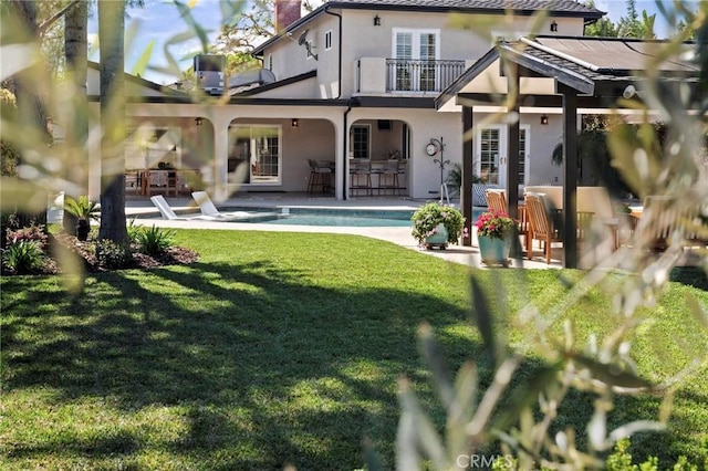 back of property featuring a balcony, an outdoor pool, a yard, a patio, and stucco siding