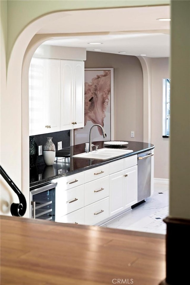 kitchen with arched walkways, dishwasher, beverage cooler, and a sink
