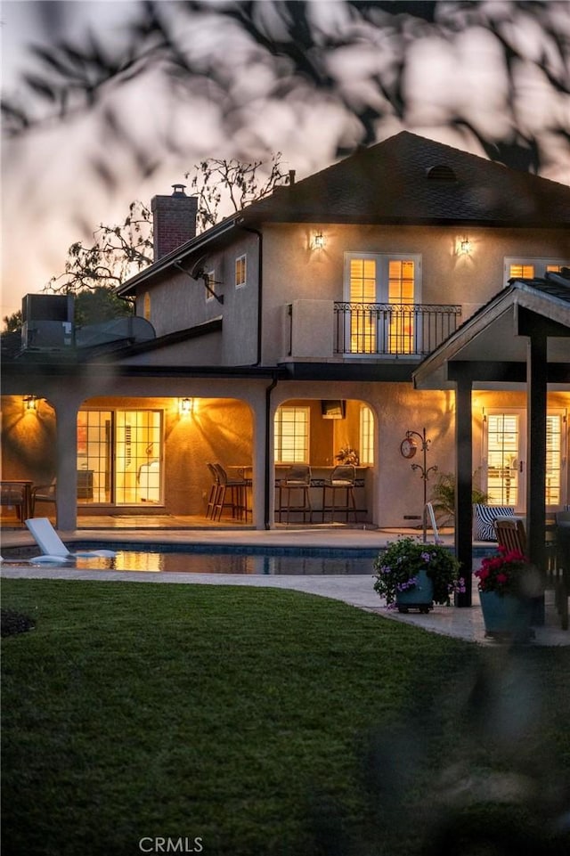 back of house featuring a chimney, a lawn, a patio, a balcony, and an outdoor pool