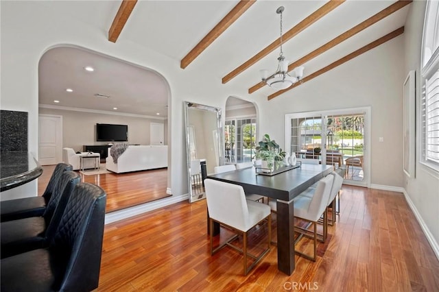 dining area featuring arched walkways, a wealth of natural light, vaulted ceiling with beams, and an inviting chandelier