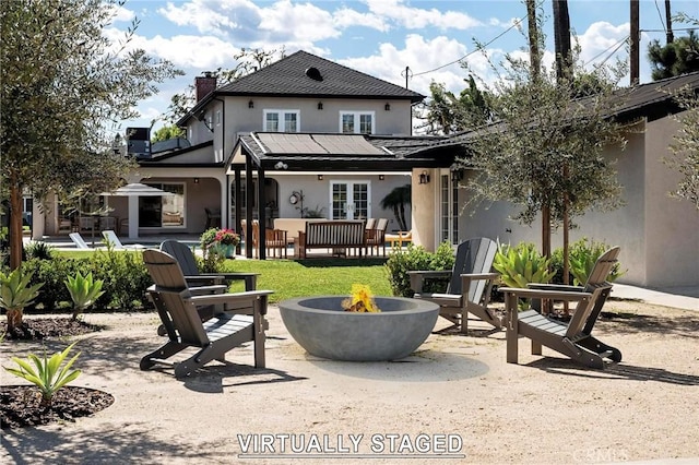 rear view of property featuring a chimney, stucco siding, a patio area, french doors, and a fire pit