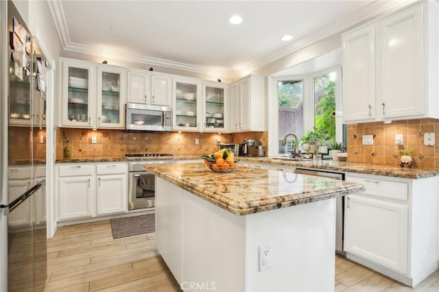 kitchen with appliances with stainless steel finishes, glass insert cabinets, white cabinetry, a kitchen island, and light stone countertops