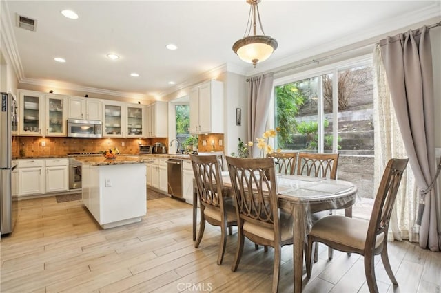 dining room featuring a healthy amount of sunlight, light wood finished floors, visible vents, and ornamental molding