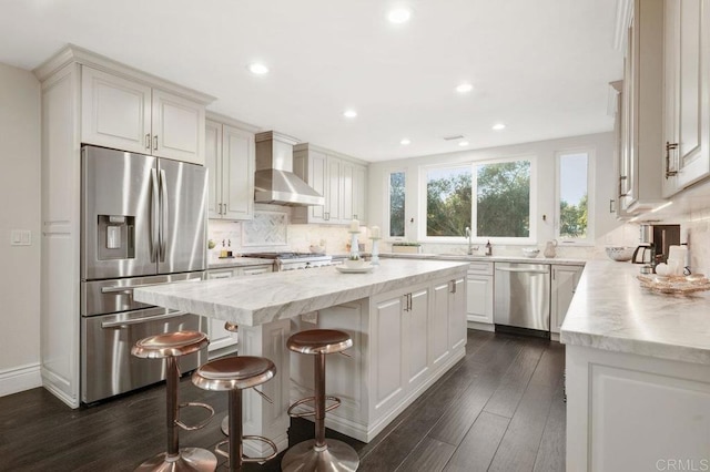 kitchen featuring a kitchen island, appliances with stainless steel finishes, wall chimney range hood, white cabinetry, and backsplash