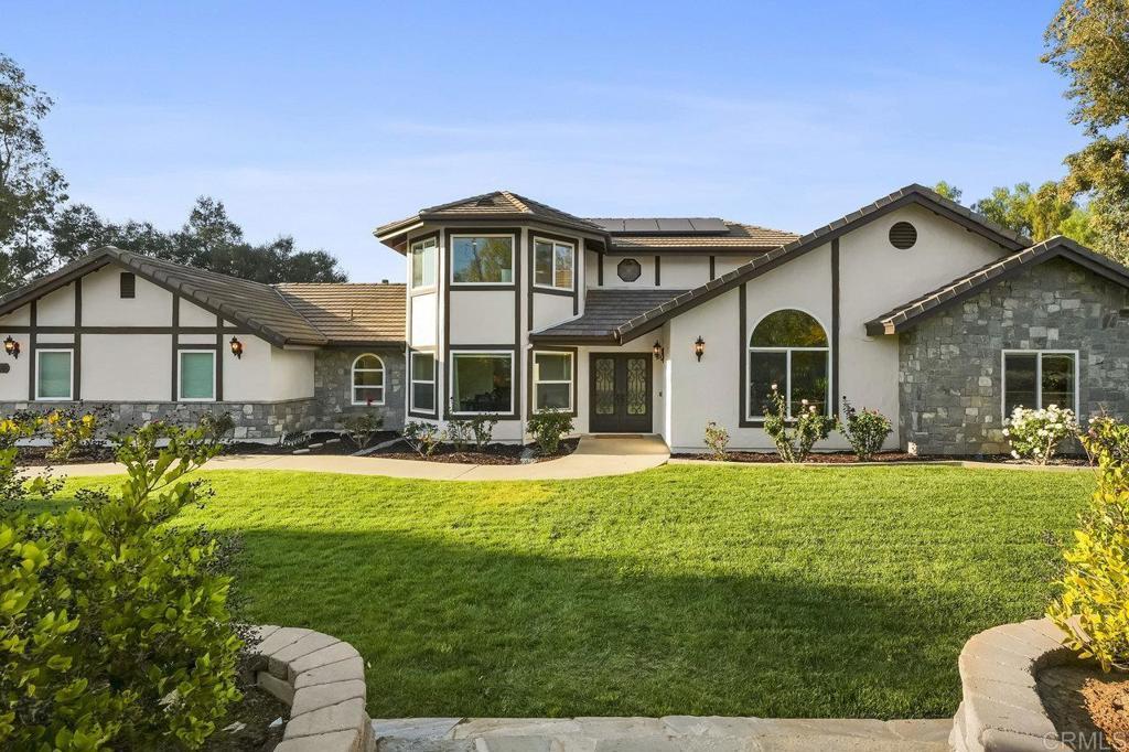 view of front of house with solar panels, a front lawn, stone siding, and stucco siding