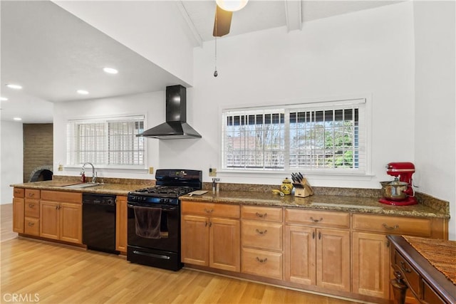 kitchen with light wood finished floors, a ceiling fan, wall chimney exhaust hood, black appliances, and a sink