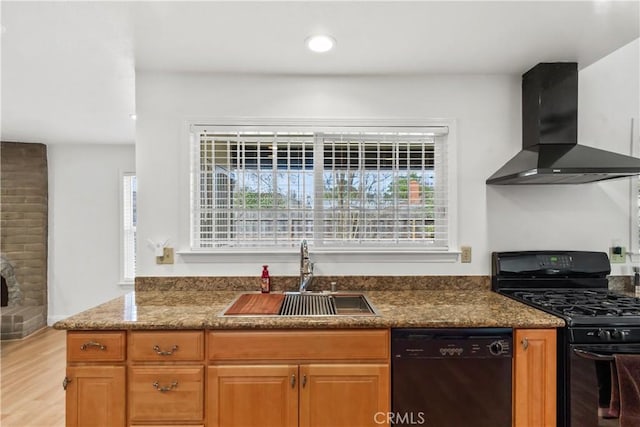 kitchen with light wood-style flooring, brown cabinetry, a sink, wall chimney range hood, and black appliances